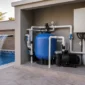 Filtro de areia azul, motobomba, tubulações PVC, registros e manômetro em casa de máquinas ao lado de piscina