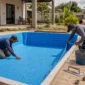Equipe técnica ajustando manta de vinil azul dentro de piscina residencial