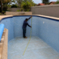 Profissional medindo uma piscina vazia para troca de vinil, com trena, pontos de retorno e rolo de revestimento azul