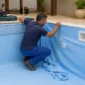 Técnico medindo revestimento vinílico azul dentro de piscina residencial com skimmer e retorno aparentes