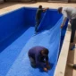 Técnicos instalando manta vinílica azul em piscina vazia durante troca de revestimento