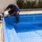 Técnico instalando manta de vinil azul em piscina residencial com ferramentas ao lado