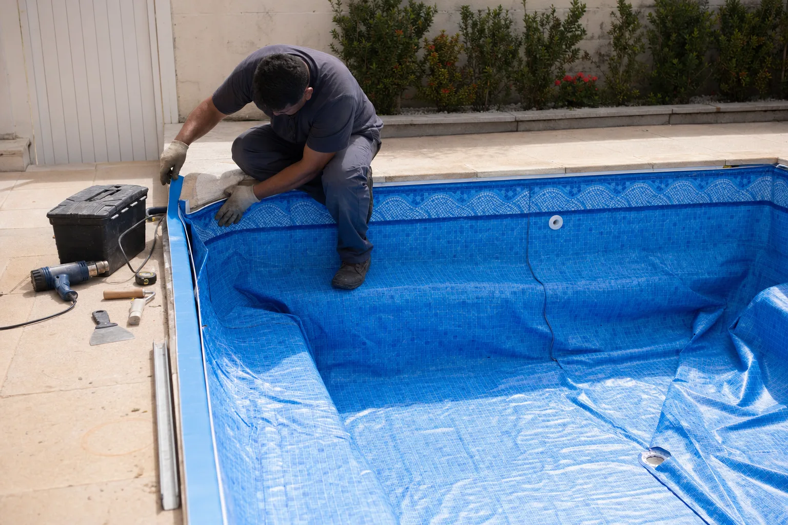 Técnico instalando manta de vinil azul em piscina residencial com ferramentas ao lado