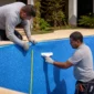Técnicos medindo revestimento de vinil azul em piscina residencial durante reforma