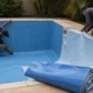 Técnicos medindo piscina de vinil durante reforma com revestimento azul parcialmente instalado
