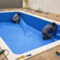 Técnicos posicionando bolsão de vinil azul em piscina residencial sem água no Setor Colina Azul