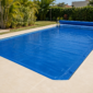 Capa térmica azul ajustada sobre piscina residencial em Professor Jamil, com rolo manual ao lado