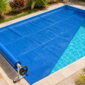 Capa térmica azul de bolhas instalada sobre piscina residencial com enrolador manual