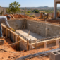 Piscina de alvenaria em construção com armadura, tubulações hidráulicas e profissional conferindo medidas em Divinópolis de Goiás