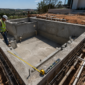 Obra de piscina de alvenaria com ferragens, tubulação hidráulica e técnicos medindo a estrutura