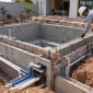 Obra de piscina de alvenaria com ferragens, tubulação hidráulica e técnicos medindo a estrutura
