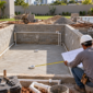 Piscina de alvenaria em construção com estrutura, tubulações hidráulicas e profissional conferindo medidas no Parque das Laranjeiras, Goiânia