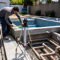 Técnico medindo piscina de alvenaria em construção com tubulações hidráulicas e dispositivos instalados