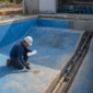Técnico inspecionando o dreno de fundo e a tubulação de sucção de uma piscina em construção em Goiânia.