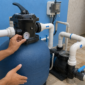 Técnico conferindo filtro de areia, bomba, manômetro e tubulações de PVC na casa de máquinas de uma piscina