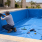 Dois técnicos instalando revestimento vinílico azul em piscina residencial vazia