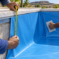 Técnico medindo revestimento vinílico azul durante troca de vinil de piscina em obra