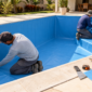 Dois profissionais instalando revestimento vinílico azul em piscina residencial vazia