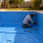 Dois técnicos instalando revestimento vinílico azul em piscina residencial vazia