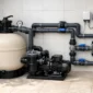 Filtro de areia, bomba, manômetro, registros e tubulações organizadas em casa de máquinas de piscina