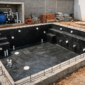 Obra de piscina de alvenaria com ferragens, tubulação hidráulica e técnicos medindo a estrutura