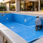 Piscina residencial em construção com revestimento de vinil azul, técnico conferindo a borda e dispositivos hidráulicos instalados
