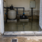 Casa de máquinas de piscina inundada com drenagem, bomba, filtro e quadro elétrico protegido.