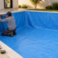 Profissional instalando revestimento de vinil azul em piscina durante atendimento técnico