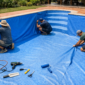 Equipe ajustando revestimento vinílico novo nas paredes de uma piscina residencial.