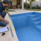 Técnico medindo revestimento vinílico azul durante troca de vinil de piscina em obra